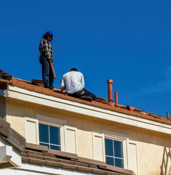 Roof construction scene with workers on a tiled roof, captured under a clear blue sky.