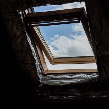 A wooden attic window opens to reveal a clear blue sky and fluffy white clouds.